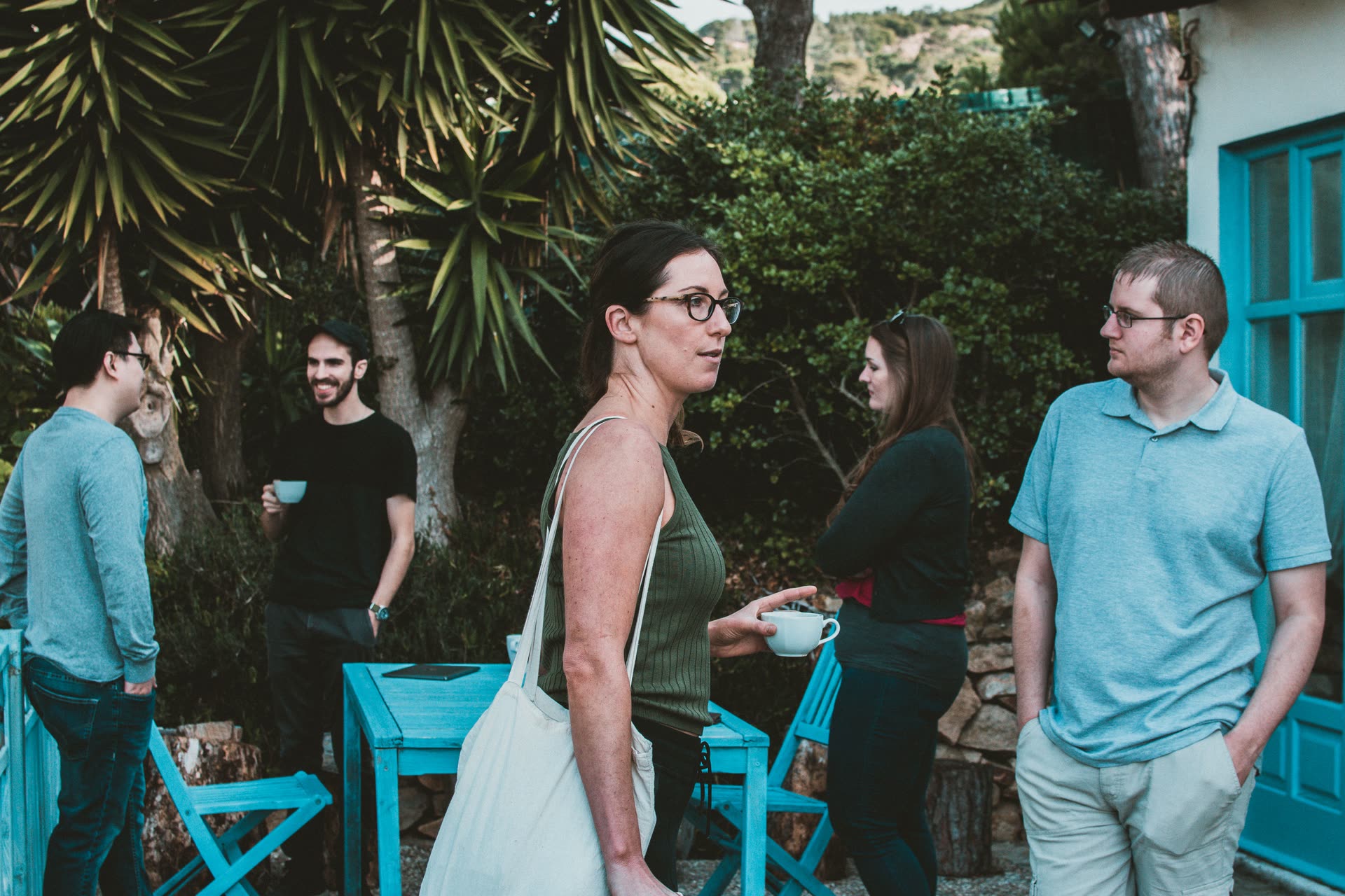 People talking in small groups over coffee on a garden patio with blue tables.