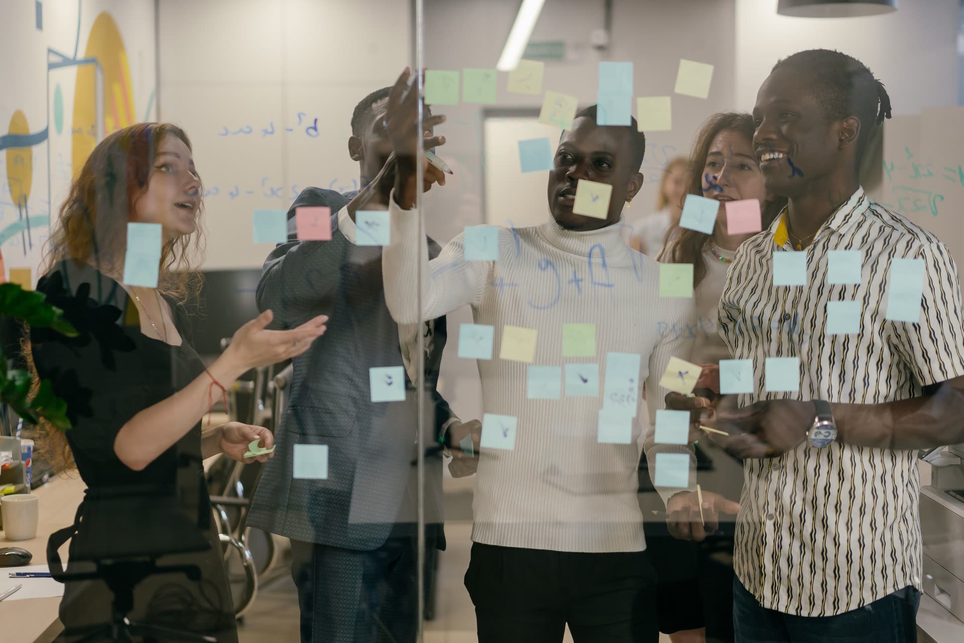 A team planning with sticky notes on a glass wall, seen through the glass.