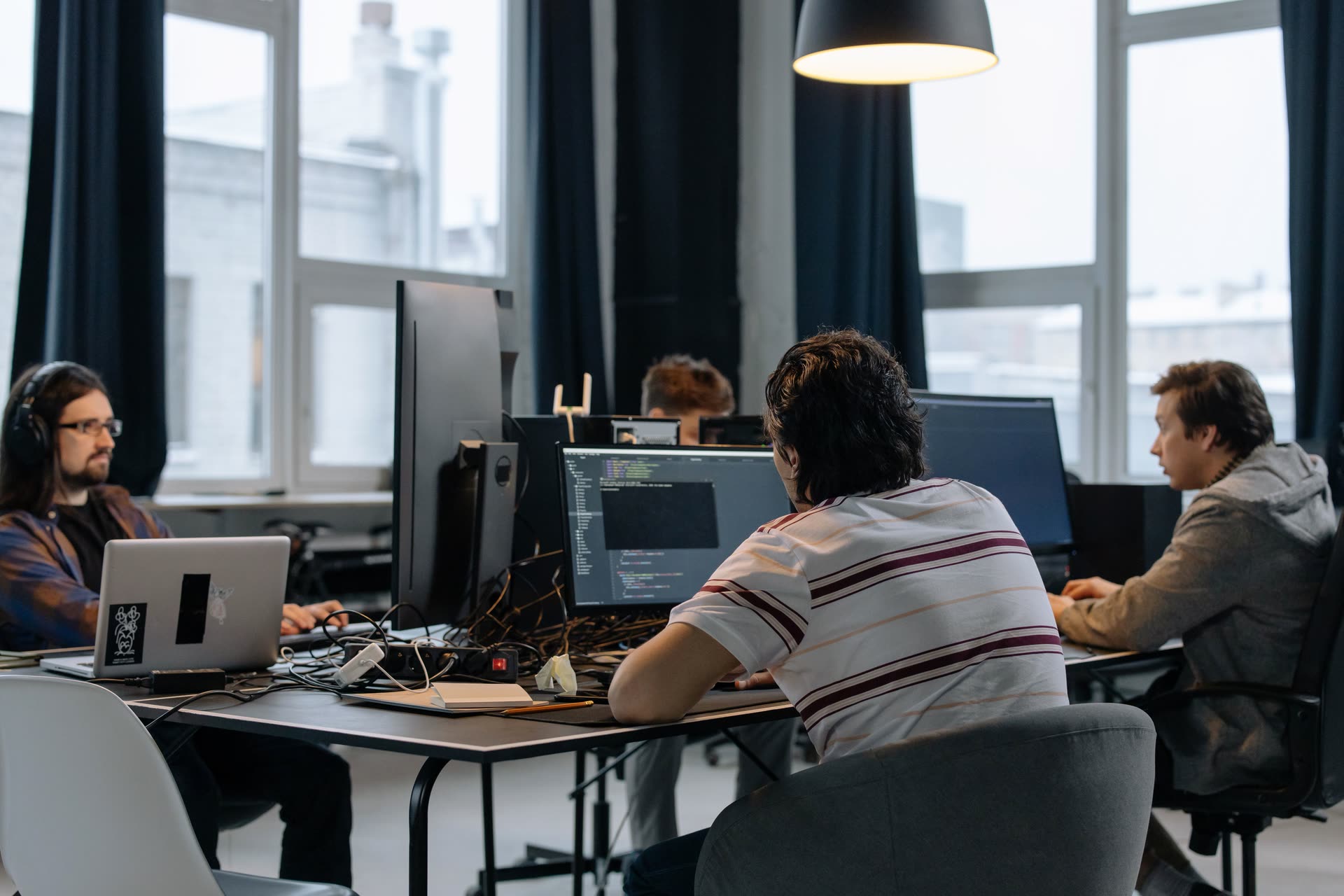 Developers working at monitors and laptops around a shared desk in a bright office.