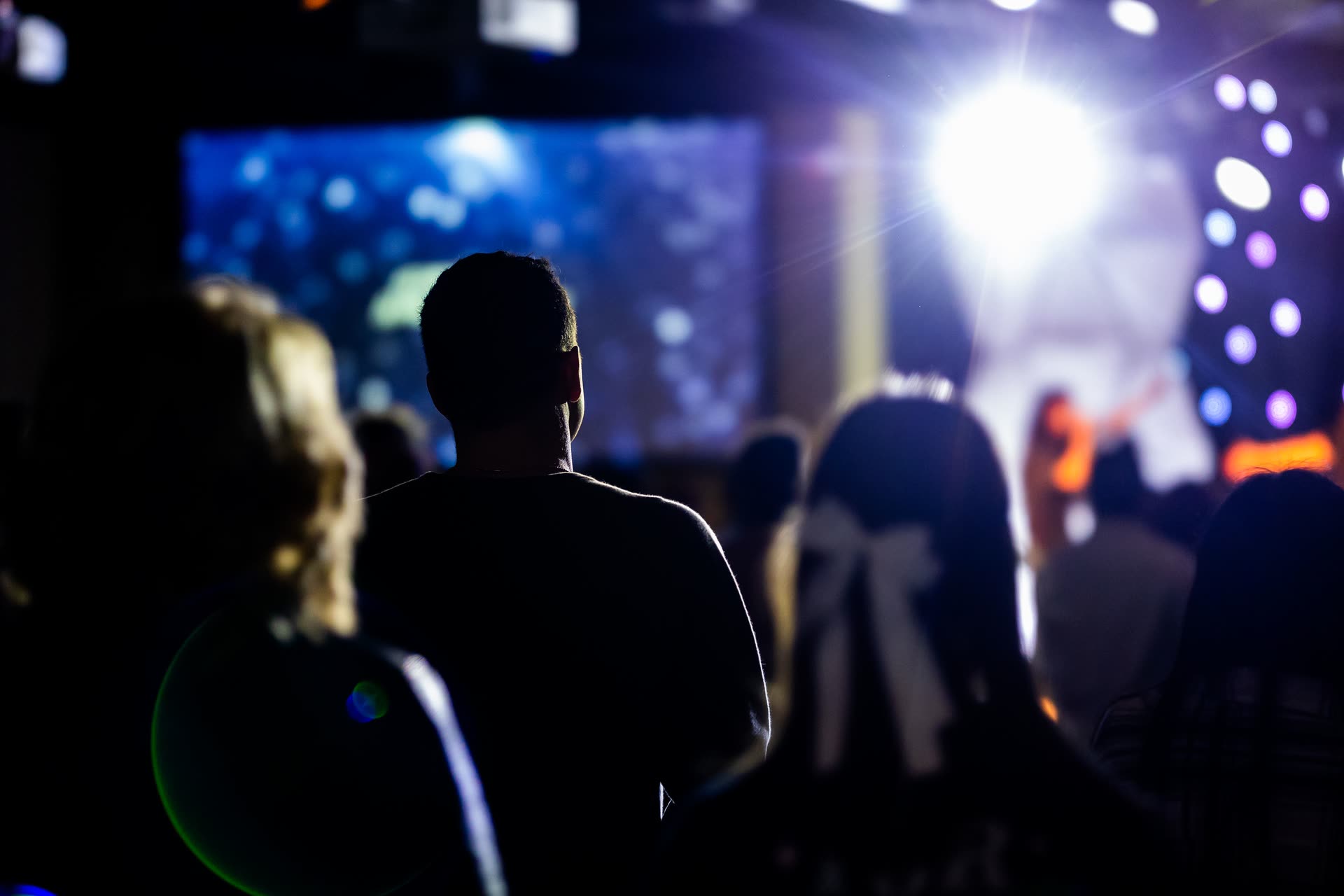 Silhouetted audience members watching a brightly lit conference stage.