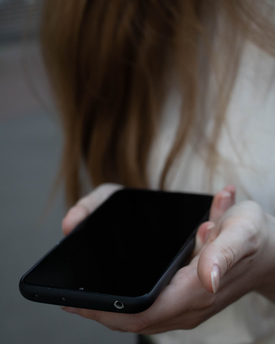 Two hands holding a smartphone with a dark, blank screen.