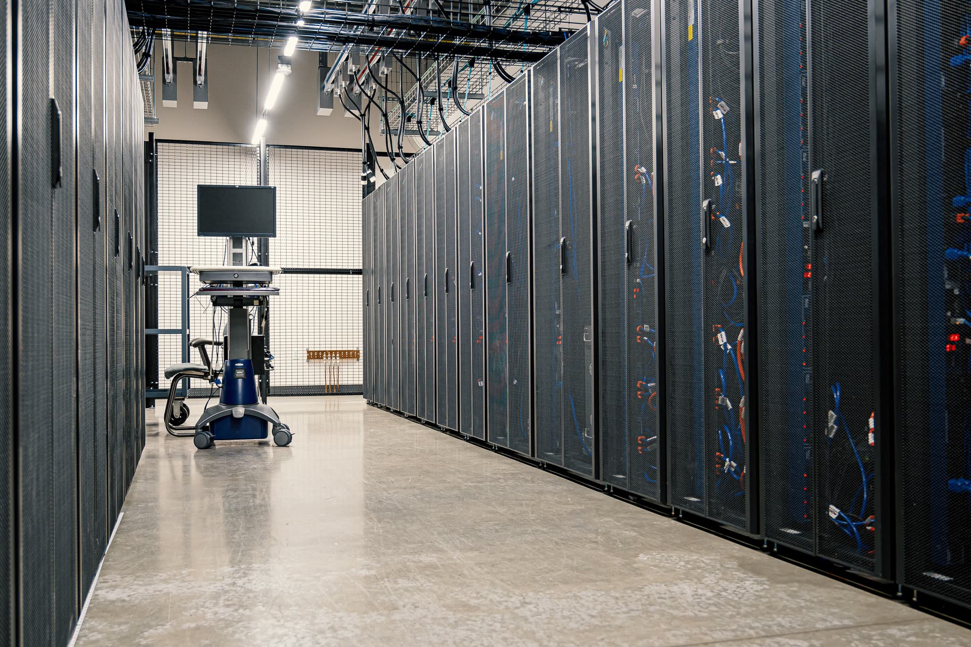 An aisle of black server cabinets in a data centre, a workstation cart at the far end.